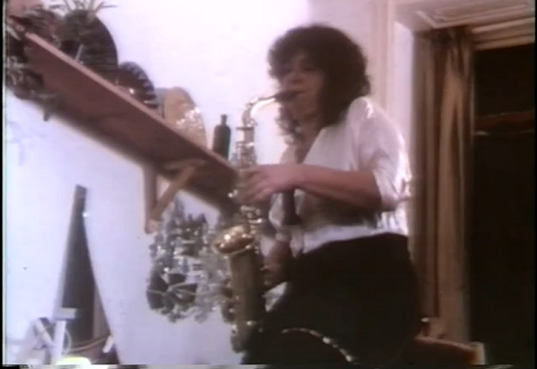 Film still in colour. Woman playing a saxophone.