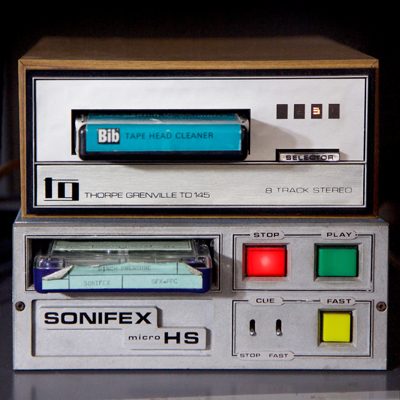 1970s-style cartridge player, brushed steel in wooden box, with blue Bib tape head cleaner cartridge inserted.