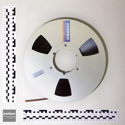 aluminium 10.5 inch reel containing quarter inch brown magnetc audio tape with rulers indicating dimensions.