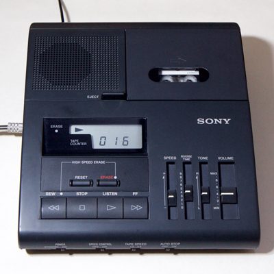 image when enlarged shows 2 machines, a portable handheld Philips 393 minicassette machine with strap and a larger desk-top Sony Microcassette machine with digital display