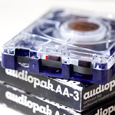end view of cartridge showing black magnetic tape and foam pressure pads, resting on Audiopak AA-3 cardboard boxes for cartridges