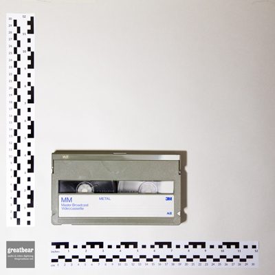 khaki-grey MII (M2) video cassette with rulers indicating width 18.7 cm by height 10.6 cm.