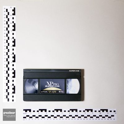dark grey rectangular S-VHS video cassette, with rulers indicating width 18.7 cm by height 10.3 cm.