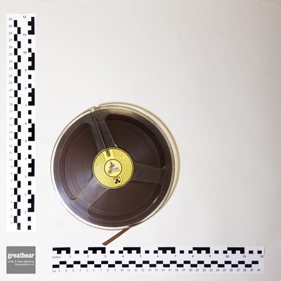 clear plastic 7 inch reel containing quarter inch brown magnetic audio tape with rulers indicating dimensions