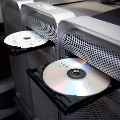 3 large silver-coloured computers with DVD-Rs loaded in their open disc drive trays