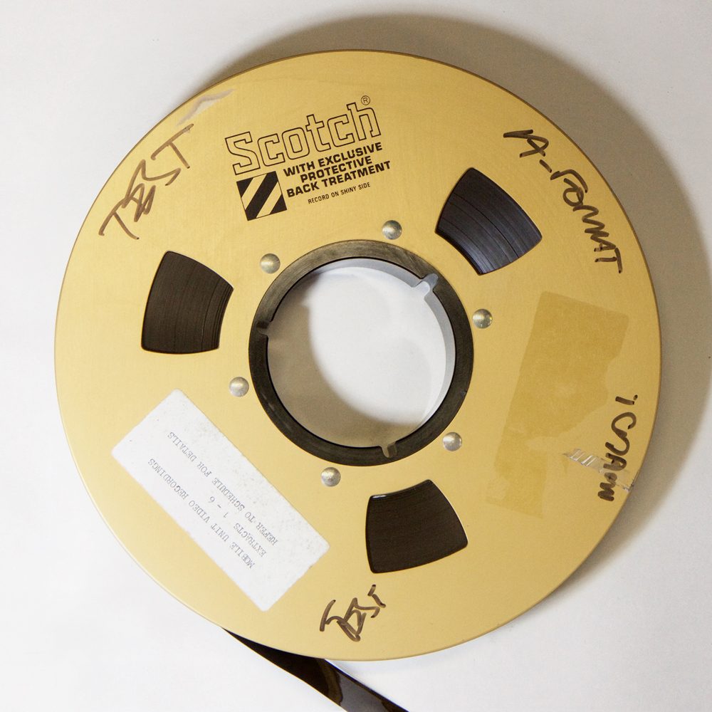 large gold-coloured tape spool with dark brown / black one inch video tape labelled: "Scotch, with exclusive protective back treatment"