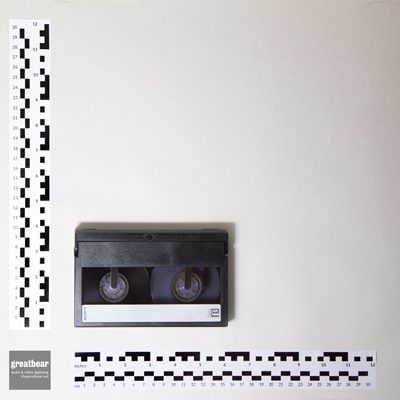 Rectangular, dark grey, plastic video cassette with rulers showing width 15.6cm and height 9.6 cm