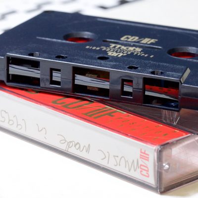 Audio Cassette showing ⅛ inch / 3.81mm black tape, resting on cassette box labelled with handwritten text: music made in 1995