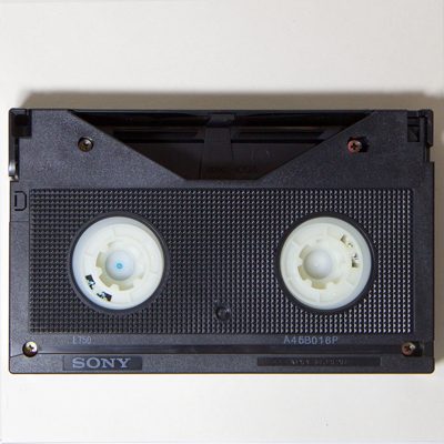 black rectangular cassette with ivory-coloured plastic reel hubs, resembling inverted cog wheels