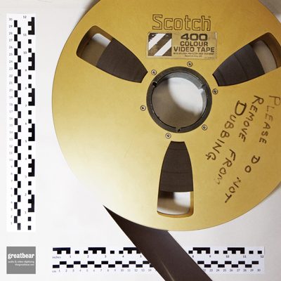 Large gold-coloured 14 inch spool with 2 inch wide dark brown quadruplex video tape and rulers indicating dimensions