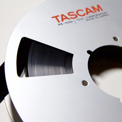 section of aluminium spool, with words: Tascam RE-1050 TEAC Corporation Made in Japan, wound with very dark brown 1 inch tape