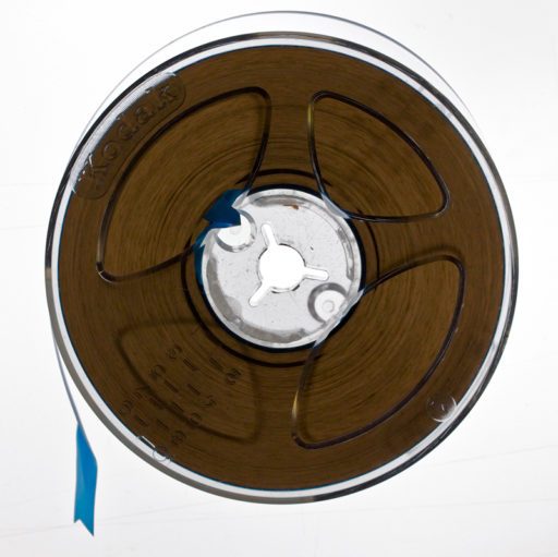 Clear plastic tape reel wound full with brown quarter inch tape, backlit to show translucence of tape