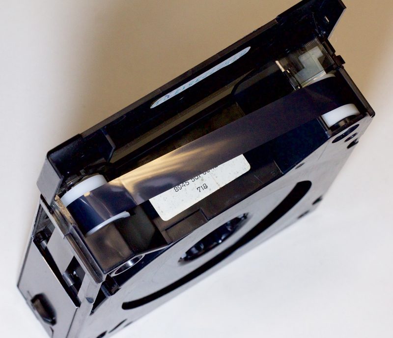 Stripe of black video tape held diagonally between two white plastic spools inside cassette housing